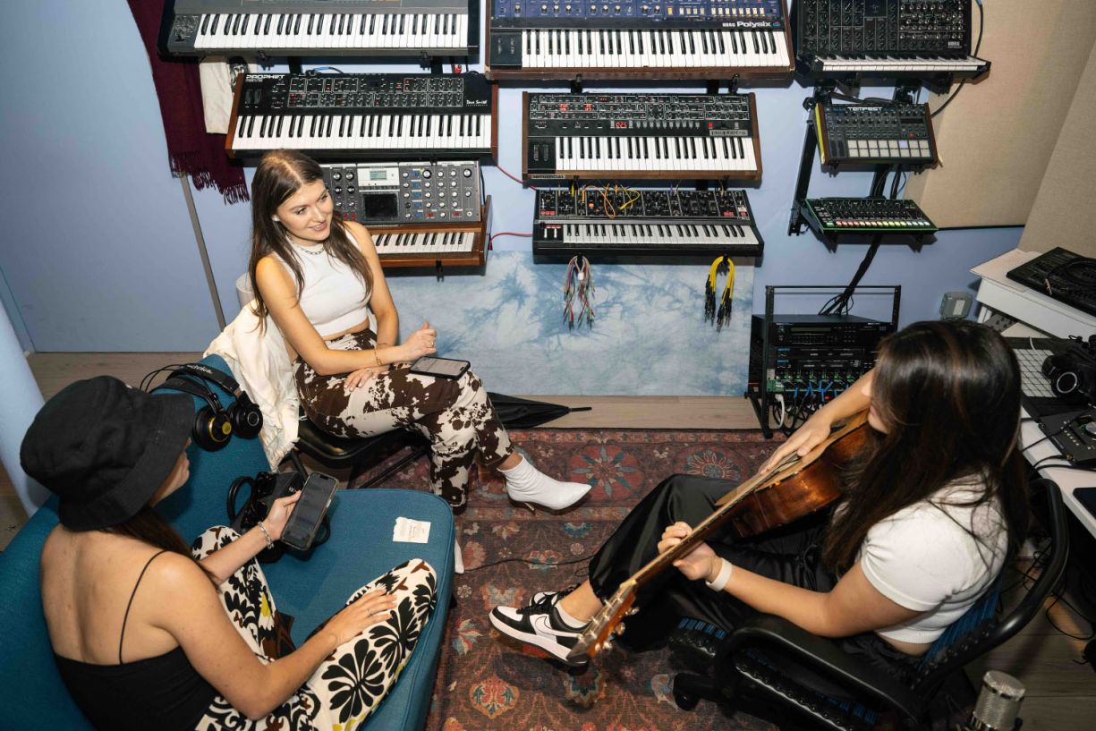 3 women in a studio sitting in front of a wall of synths